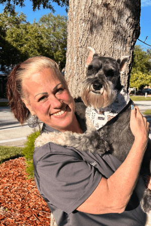 Elise Gruber female standing by a tree holding a Schnauzer wearing a bandana