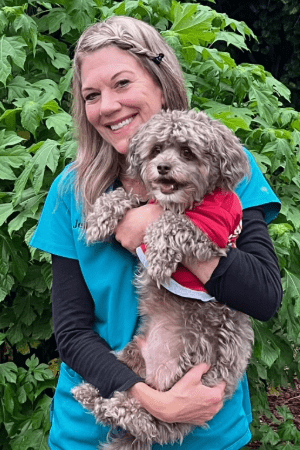 Jennifer Jordan Female with long blonde hair braded in the front holding a small gray dog with curly hair wearing a red shirt