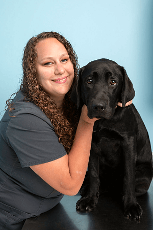 Female with long curly brown hair posing with a black Labrador