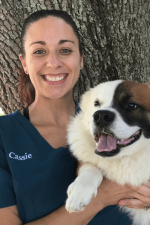 Cassie Joyner female with brown hair in pony tail posing with large fluffy dog in front of tree