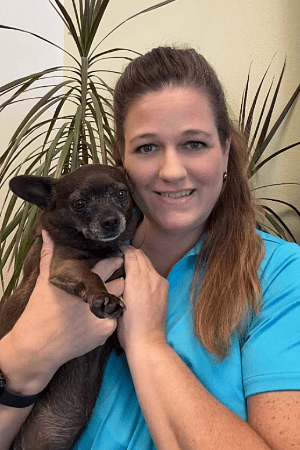 Julie female with long brown hair wearing a baby blue shirt and holding a small black dog