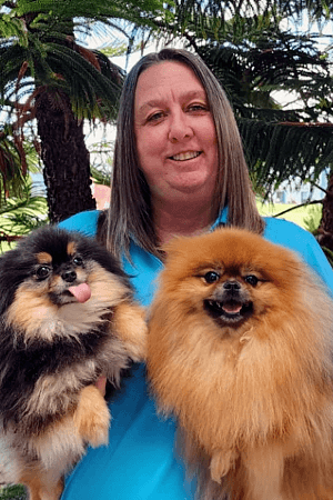 Tammy Female with shoulder length brown hair holding two Pomeranian dogs